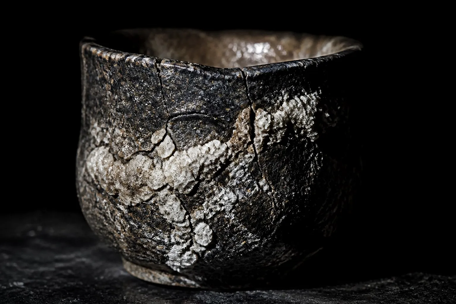 Editorial illustration: An ancient cracked ceramic drinking cup with dried salt crust, lit like a relic on black slate