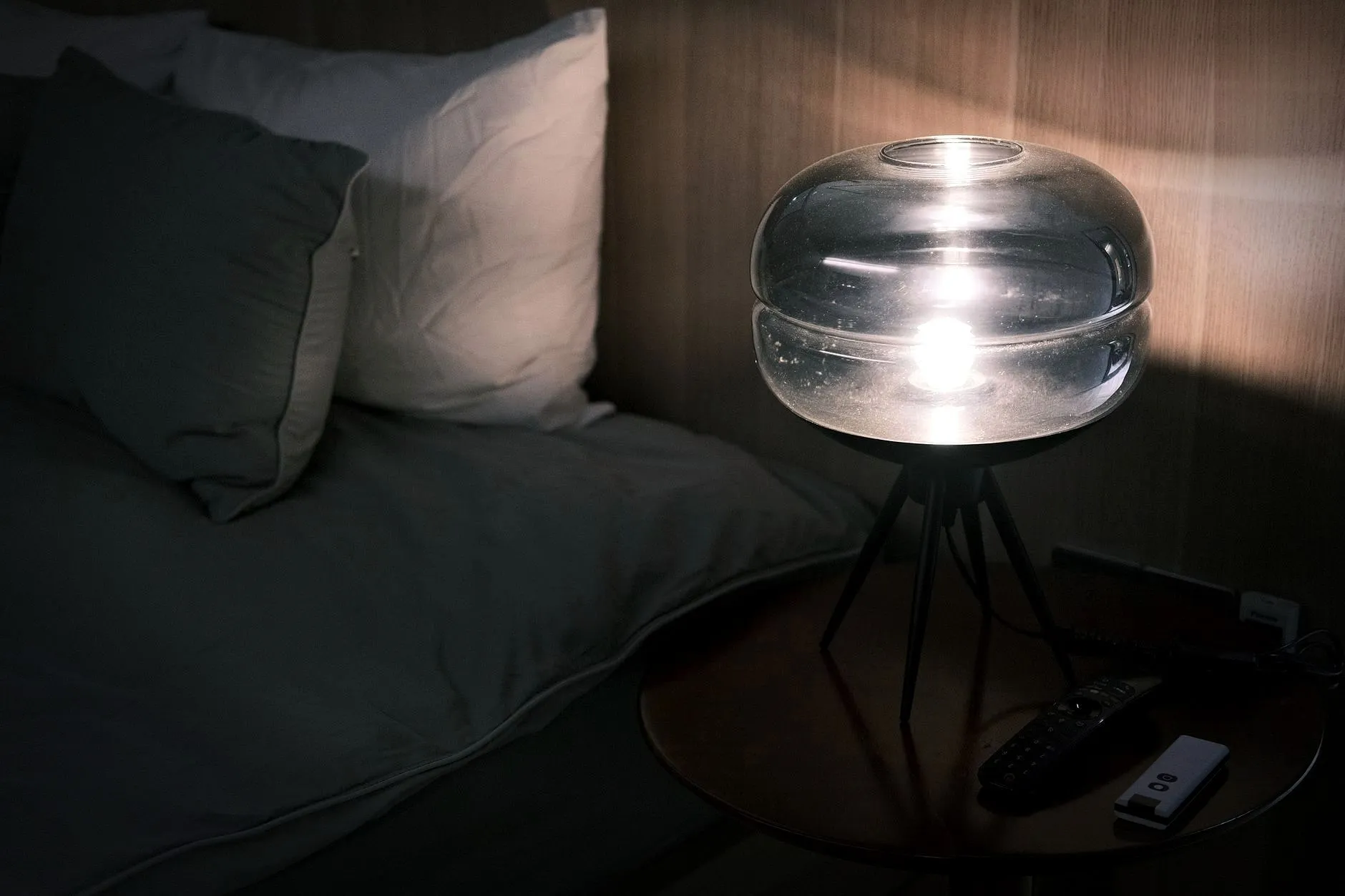 Illuminated bedside table with modern glass lamp and pillows at night.