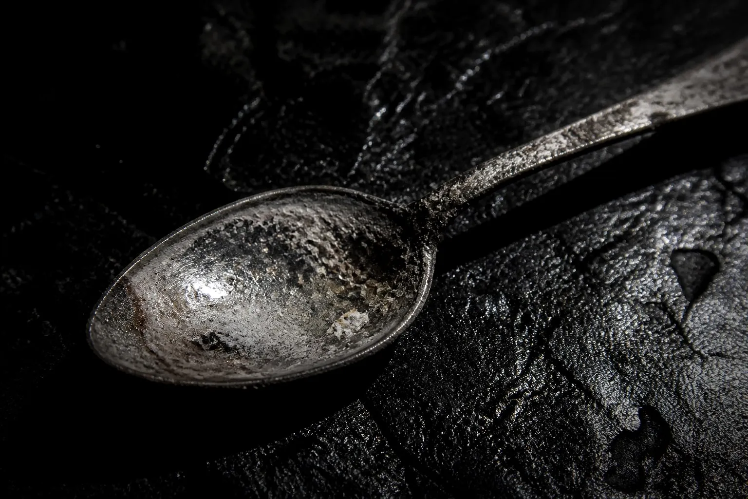 Editorial illustration: A dented silver teaspoon coated in chalky toothpaste residue, lit like a forensic relic on black