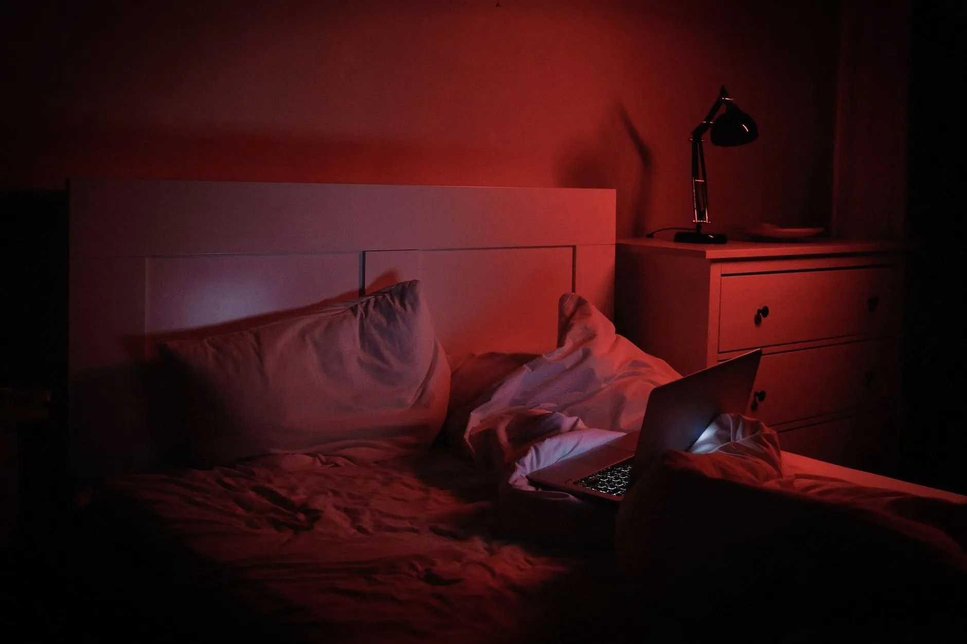 A dimly lit bedroom scene featuring a cozy bed with a laptop and a warm ambiance.